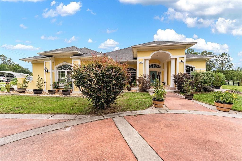 Front elevation of the residence, a butter-yellow Mediterranean facade with a columned arched portico and circular brick drive