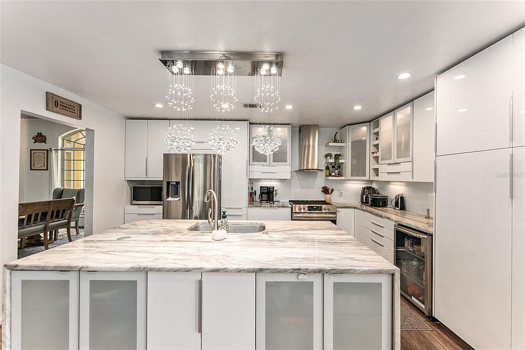The chef's kitchen with a quartzite waterfall island, glossy white cabinetry, and bubble-cluster crystal pendants overhead