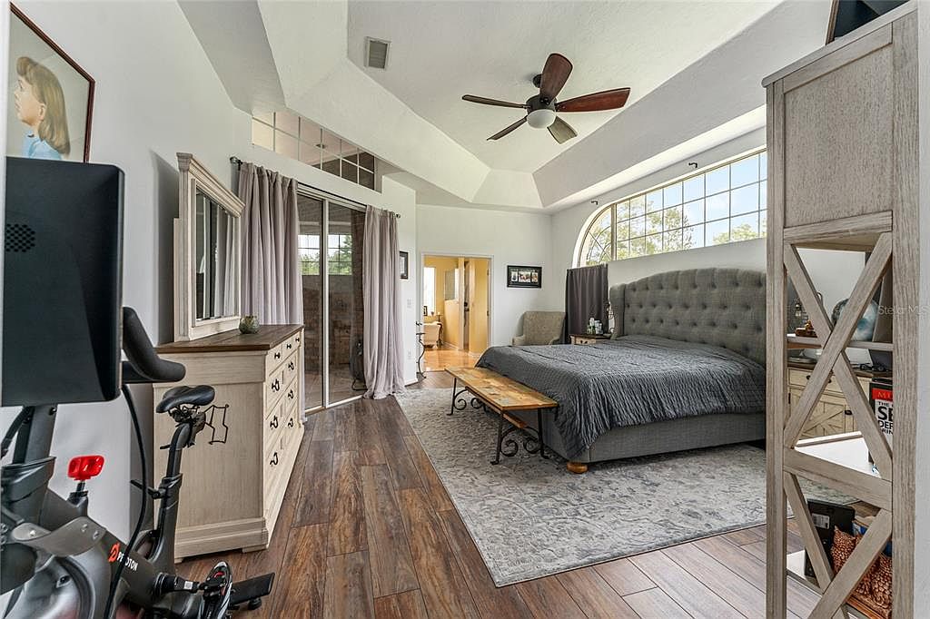The primary suite with a tray ceiling, arched feature window, and a tufted upholstered headboard