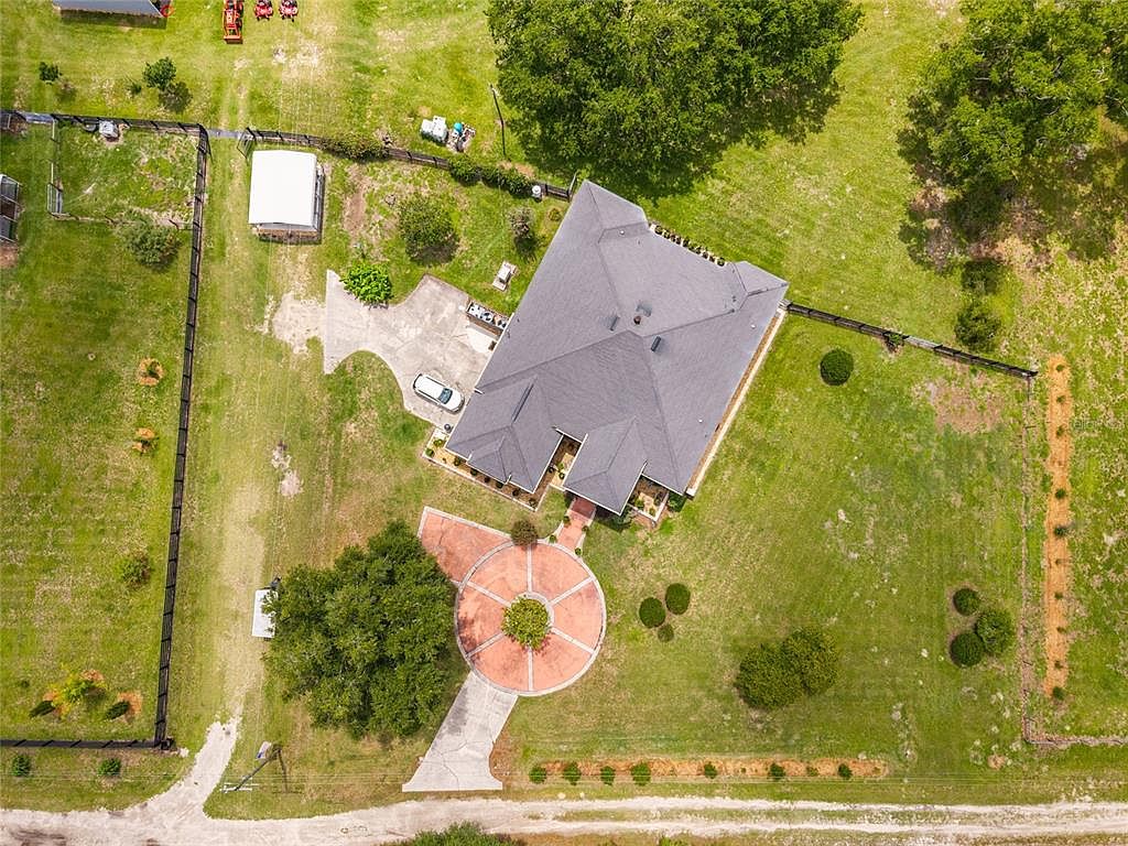 Top-down aerial of the residence at the center of the circular pattern-stamped drive, with mature trees and the geometry of the 15-acre lot visible