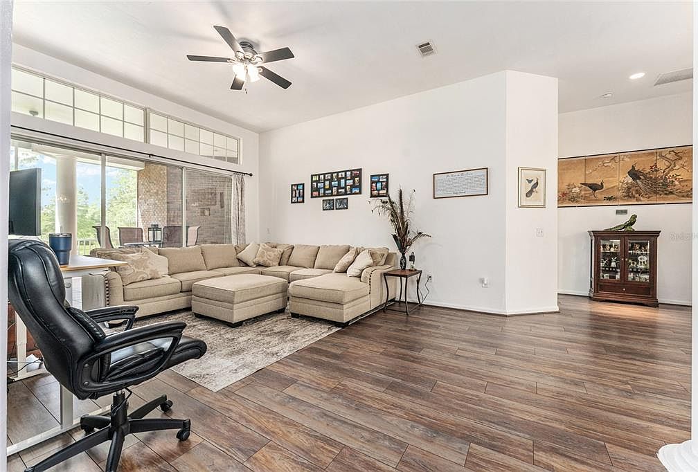 The great room with a wide sectional, a wall of glass sliders leading to the screened lanai, and warm wood-look flooring