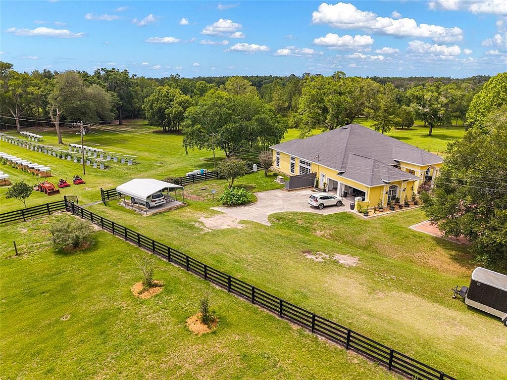 Oblique aerial of 15510 SW 149th Pl: the Mediterranean residence anchors the foreground while the white-fenced pastures and outbuildings stretch back across the fifteen-acre parcel of North Central Florida farmland